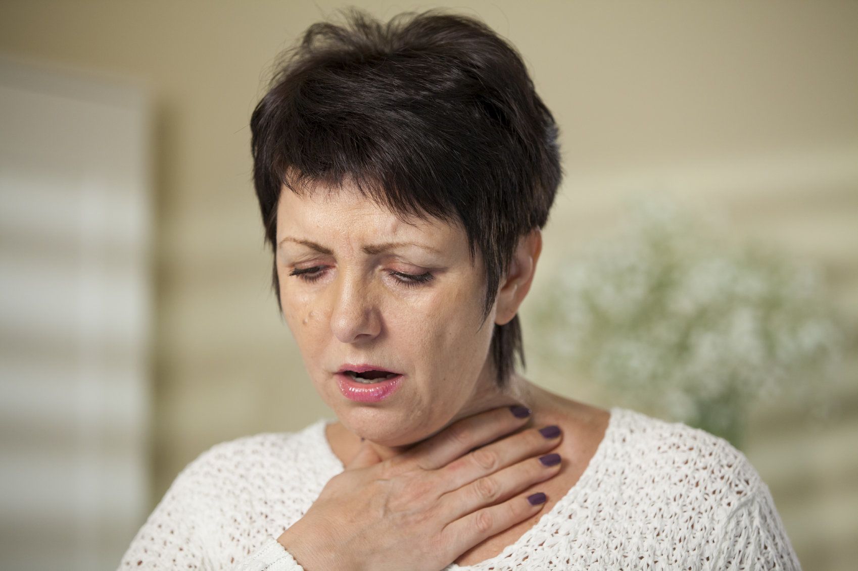 A dark-haired woman feeling her throat